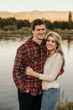 a couple standing next to each other in front of a body of water at sunset