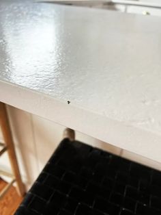 a white counter top in a kitchen next to a bar stool and table with black tile on it