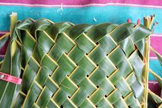 a woven basket is sitting on a colorful blanket with pink ribbon around the edges and green leaves