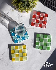 four different colored glass tiles sitting on top of a white table next to a potted plant