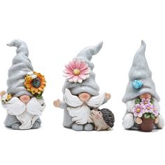 three gnome figurines sitting next to each other with flowers in their hair and one holding a hedge