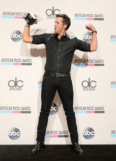 a male in a black shirt is holding his hands up while standing on the red carpet