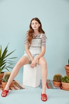 a young woman sitting on top of a white block next to potted plants and books