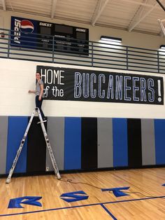 a man standing on a ladder in front of a sign that reads home of the bucaneers