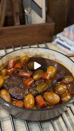 a pot filled with meat and vegetables on top of a stove burner next to a stack of books