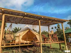 a tent set up in the middle of a field with chairs and tables under it