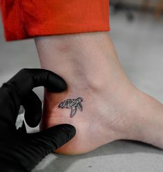 a small tattoo on the foot of a person wearing black gloves and holding a glove