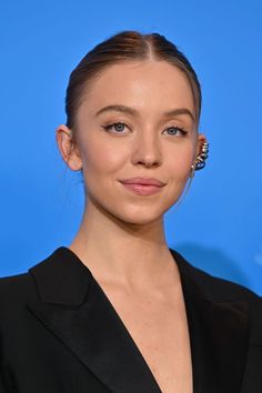 the actress is posing for a photo in front of a blue background with her hair pulled back