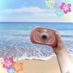 a person holding up a pink camera in front of the ocean with flowers on it