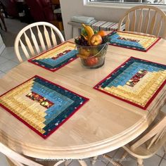 a wooden table topped with a bowl of fruit and two place mats on top of it