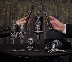 two people holding candles with skulls on them and wine glasses in front of the candle holders