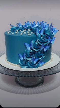 a blue cake decorated with flowers and pearls on a silver platter next to a white plate