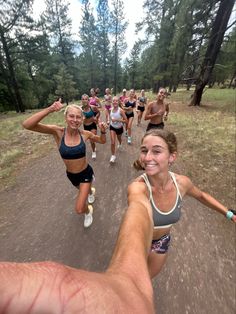 a group of people running down a dirt road in the woods with trees behind them