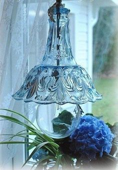 a glass light hanging from a window next to a blue carnation and green plants