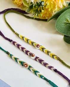 three braided bracelets sitting on top of a table next to flowers and leaves