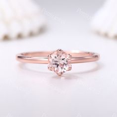 a pink diamond ring sitting on top of a white table next to some seashells