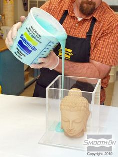 a man pouring blue liquid into a cup on top of a white table next to a statue