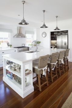 a kitchen with an island and chairs in the center, along with white walls and wood flooring