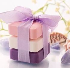 three soap bars wrapped in purple ribbon and sitting on top of each other next to flowers