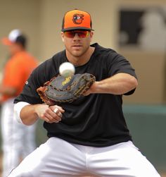 a man in black shirt and white pants holding a baseball mitt with orange visor