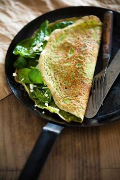 an omelet on a black plate with a fork and knife