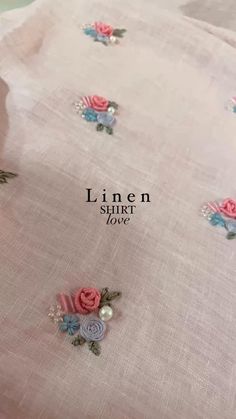 linen shirt with pink roses and pearls on it, sitting on top of a table