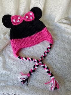 a crocheted minnie mouse hat laying on top of a white bed with pink and black trim