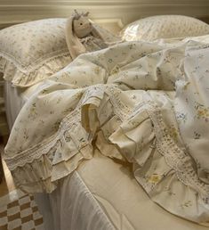 an unmade bed with white ruffles and pillows on top of the sheets