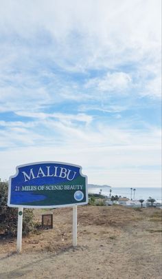 a blue sign sitting on the side of a dirt road next to the ocean and palm trees