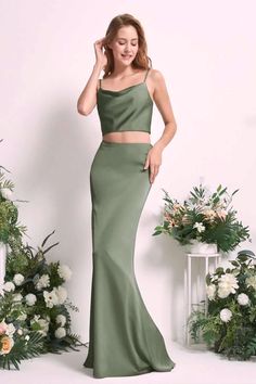 a woman standing in front of flowers wearing a green two piece skirt and crop top