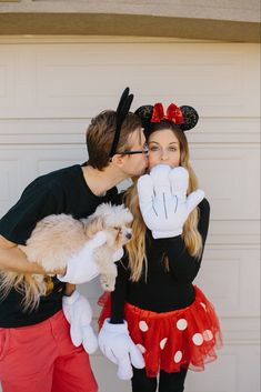 a man and woman dressed up as mickey and minnie kissing each other while holding a small dog