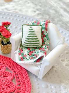 a crocheted christmas tree sits on a chair next to a potted plant