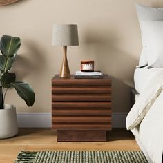 a bedroom with a bed, nightstand and plant on the side table in front of it