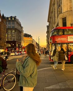 a red double decker bus driving down a street next to tall buildings with people walking on the sidewalk