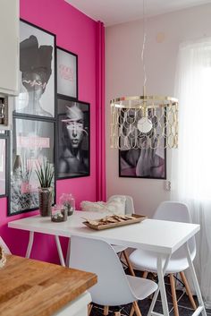 a dining room with pink walls and pictures hanging on the wall, along with white chairs