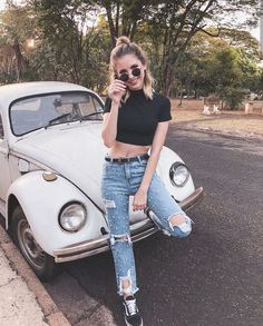 a woman sitting on the hood of an old vw beetle car while taking a selfie