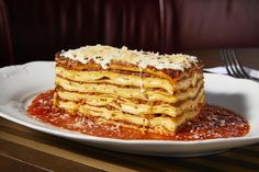 a stack of lasagna sitting on top of a white plate covered in sauce