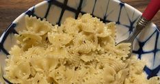 a blue and white bowl filled with pasta on top of a wooden table next to a red spoon