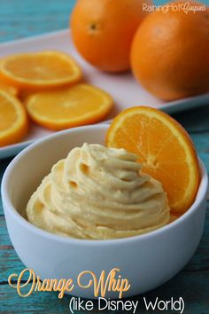 an orange whip in a white bowl next to sliced oranges on a blue table