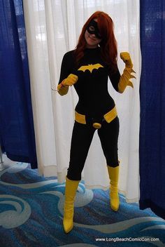 a woman dressed as batgirl standing in front of a window with blue drapes