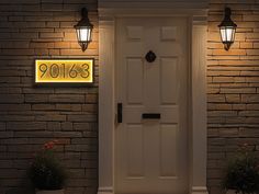 a white front door with two planters on either side and an illuminated address sign above it