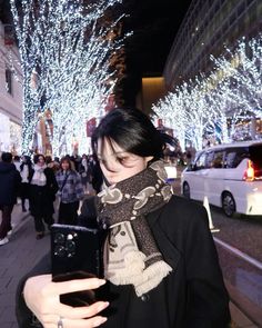 a woman is standing on the street looking at her cell phone while wearing a scarf