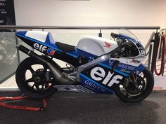 a blue and white motorcycle parked on top of a carpeted floor next to a glass wall