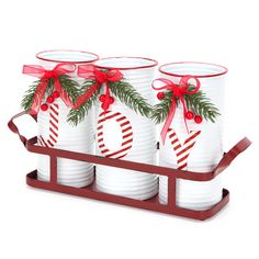 three white cups with red bows and ribbons on them are sitting in a wooden holder