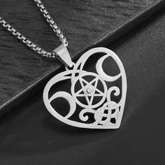 a silver heart shaped pendant with an inverted pentagramil in the center on a black surface