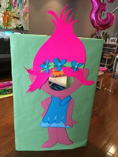 a cardboard cut out of a cartoon character with pink hair and blue dress, standing on a wooden floor