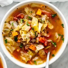 two bowls of vegetable soup with spoons on a marble counter top next to napkins