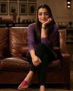 a woman sitting on a brown couch with her hand under her chin and looking at the camera