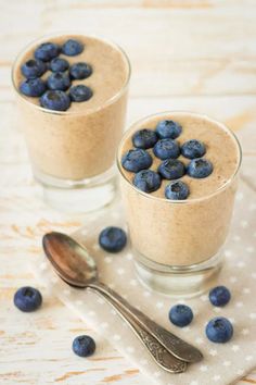 two small glasses filled with blueberries and oatmeal on a napkin next to spoons