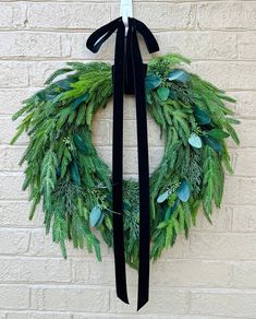 a green wreath with black ribbon hanging on a brick wall